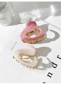 Detail of pink and white enamel heart hair claws with golden metal teeth on white paper
