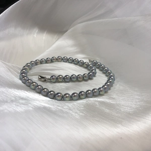 Detail view of Akoya style blue-grey pearl necklace on soft white silk fabric background