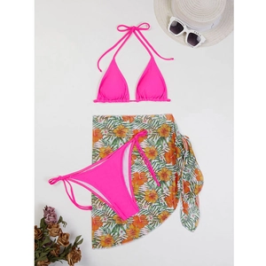 Flat lay of pink three-piece bikini set with floral print sarong and beach accessories