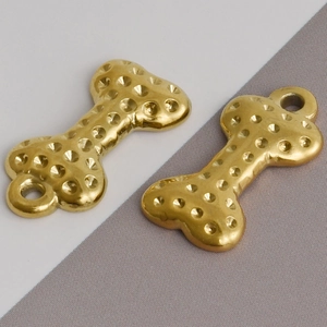 Detailed view of two gold dog bone pendants with textured surface for DIY jewelry