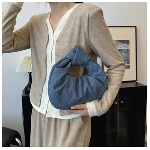 Detail of a dark blue denim dumpling bag featuring a minimalist knotted handle on model
