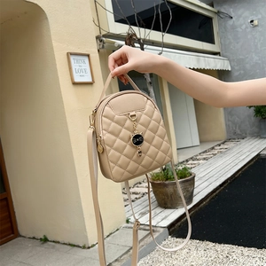 Close-up of beige quilted backpack with black cat pendant held in a street setting