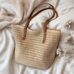 Large straw tote bag with brown leather handles on a minimalist beige fabric background