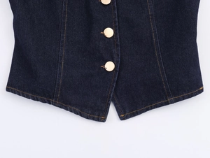 Détail du gilet en jean bleu foncé avec surpiqûres orange et boutons dorés en métal