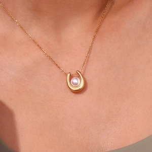Detail of 18K gold-plated horseshoe pendant with white pearl worn on female model's neck