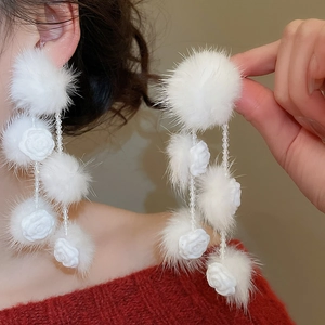 Macro detail of white pompom flower earrings with long crystal tassels on model