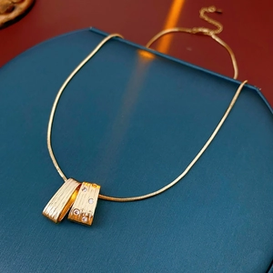 Macro detail of gold snake chain necklace with brushed geometric zircon pendant