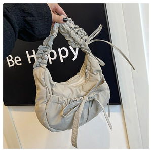 Detail of beige pleated cloud bag featuring decorative side ribbons and ruched handle