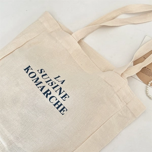 Detail of cream canvas tote bag with blue lettering on white marble background