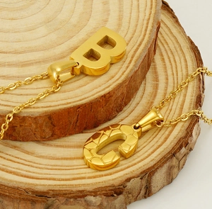 Detailed shot of 18K gold letter B and C pendants on rustic wood stack base