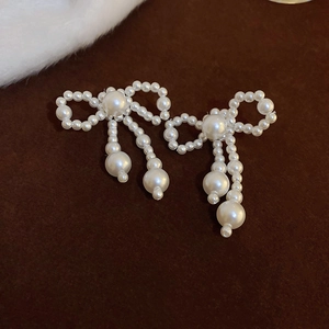 Elegant bowknot faux pearl tassel earrings with creamy white finish on a brown backdrop