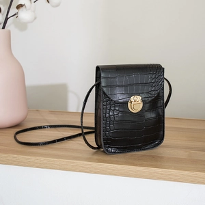 Elegant black crocodile pattern crossbody bag with a round gold metal buckle on wood