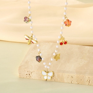 Detail view of a pearl necklace with golden butterfly, bee, and flower charms on a stone