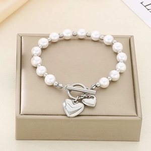 Detail view of pearl bracelet with OT buckle and silver heart pendants on gold box