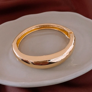 Vue macro détaillée d'un bracelet jonc doré poli avec fermoir charnière sur soie