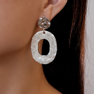 Close-up of model wearing silver hammered texture oval drop earrings with geometric design