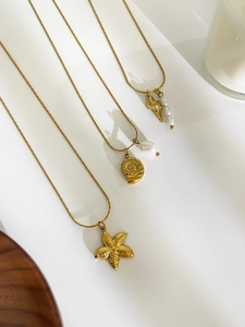 Detail of gold starfish, nautilus, and pearl pendant necklaces on a white background