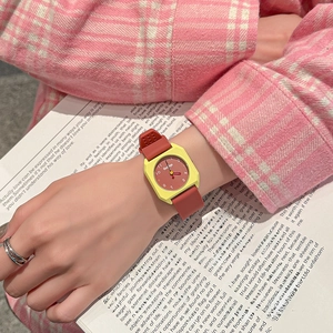 Octagonal yellow case watch with red silicone strap on wrist over a book