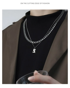 Close-up of double-layered silver Cuban chain necklace with artistic letter pendant on model