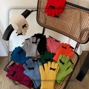 Colorful knitted touchscreen gloves with black bow accent displayed on a wooden chair