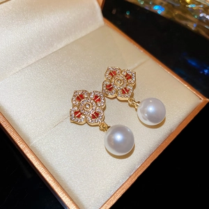 Macro detail of vintage floral gold earrings with red stones and dangling pearls