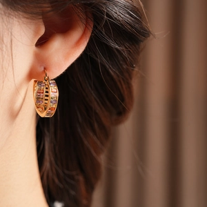 Close-up of vintage gold hoop earring with colorful rectangular gems worn by a model