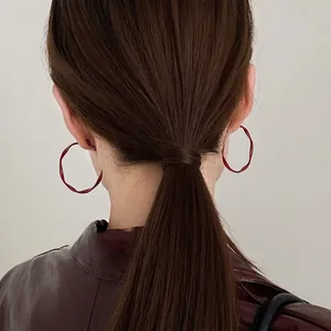 Macro detail of red geometric twisted hoop earrings worn with a chic leather jacket