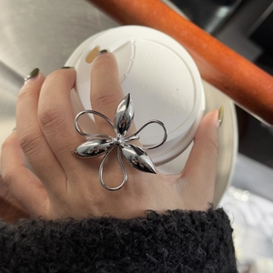 Close-up of a large silver floral ring worn by a model holding a coffee cup