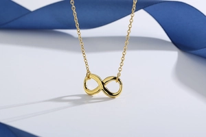 Detailed view of a gold infinity necklace with a fine O-chain on a blue ribbon background