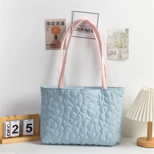 Detail of light blue quilted tote bag with floral stitching and pink handles in a cozy setting