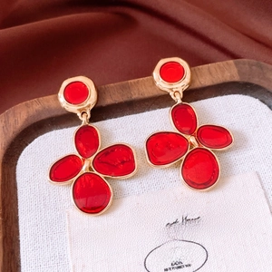 Detailed view of vintage gold-rimmed red flower earrings on a textured fabric