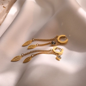 Macro shot of gold-plated leaf drop earrings with a chain and diamond accent on silk