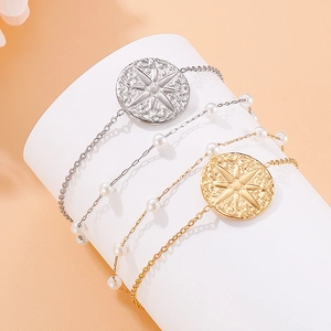 Double-layer stainless steel bracelet with pearls and sunburst charms on white pedestal
