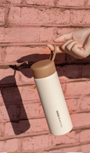 Detail of matte cream insulated bottle with brown silicone handle held against brick wall