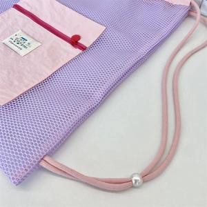 Détail d'un sac à cordon en filet violet avec poche zippée rose et perle de réglage