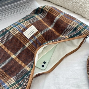 Detail view of brown plaid woolen pouch showing metal zipper and internal storage space