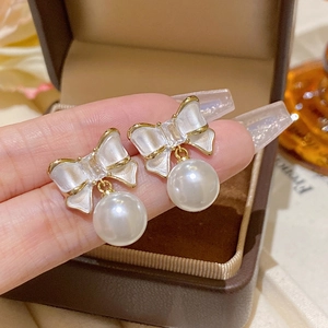 Macro detail of sweet bow earrings with white enamel gold edges and a hanging pearl