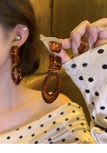 Close-up of amber resin geometric earrings showing dark brown square and circle links