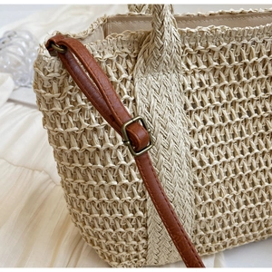 Detail of straw woven tote showing fine texture and brown PU leather strap with metal buckle