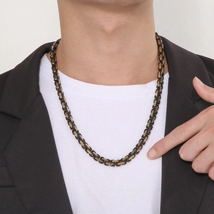 Close-up of a black and gold Byzantine chain necklace on a male model wearing a black blazer