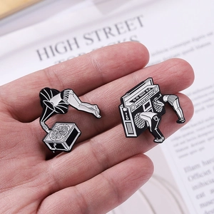 Detail of surrealist black and white enamel pins showing hands playing a vintage gramophone