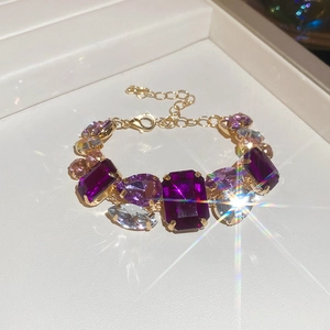 Detailed view of golden bracelet with purple and blue crystals on a jewelry tray