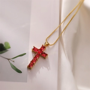 Detail of gold cross pendant with red baguette zircons on a delicate gold chain necklace