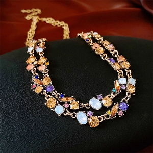Close-up of double-layer gold necklace with colorful crystals on dark silk background