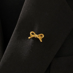 Detailed view of a gold bow brooch pinned to a black suit lapel for elegant styling