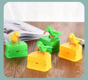 Set of four cute bird-shaped toothpick holders in green and yellow on a wooden table