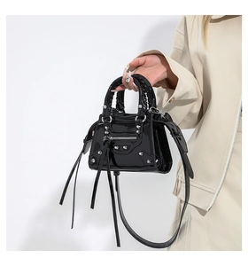 Detail of black glossy small square bag with stud accents and long tassel zipper