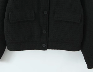 Detail view of black knit cardigan featuring button closure, pockets and woven texture