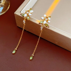 Dettaglio di orecchini a fiore in smalto dorato con pietre verdi e catenelle