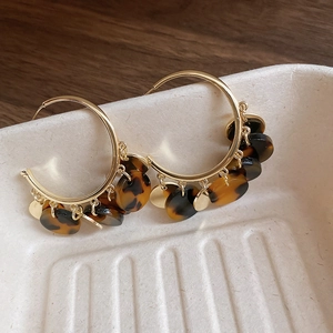 Close-up of leopard resin hoops with golden round pendants and tortoiseshell accents